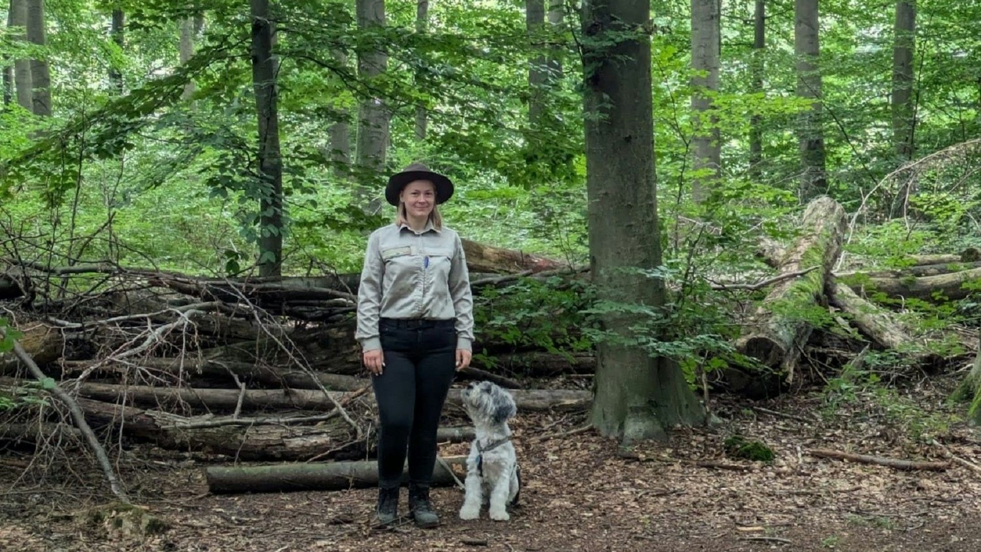 Auf dem Bild ist eine Waldhüterin mit ihrem Hund zu sehen.