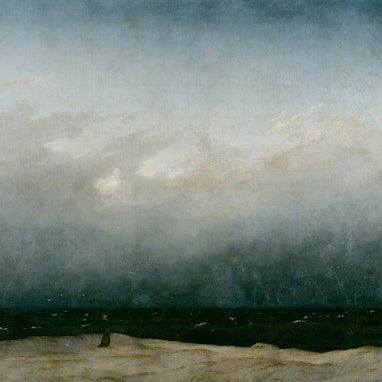 Ein Mönch steht am Strand, er wirkt sehr klein im Verhältnis zur Natur.