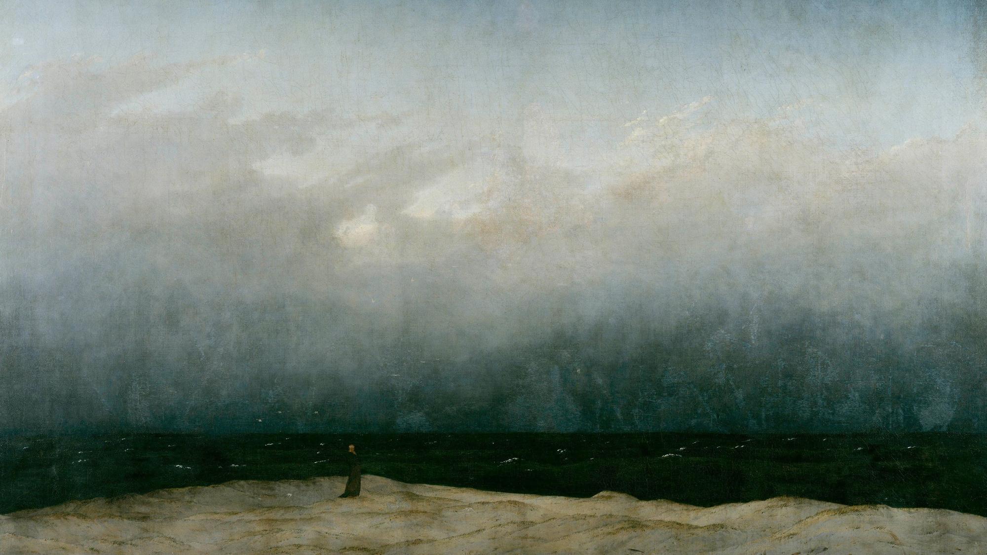 Ein Mönch steht am Strand, er wirkt sehr klein im Verhältnis zur Natur.