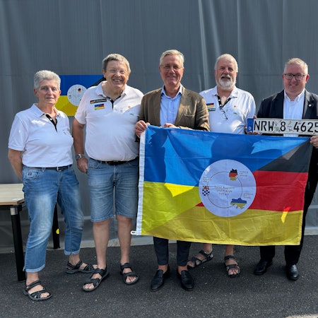 Norbert Röttgen MdB, Gunther Maassen (Vorsitzender von Sankt Augustin and friends hilft e.V.) und Sascha Lienesch MdL hinter der Fahne, mit weiteren Mitgliedern des Vereins, Ukraine