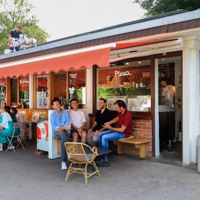 Das Büdchen am Südpark, davor sitzen einige Leute auf Bänken.