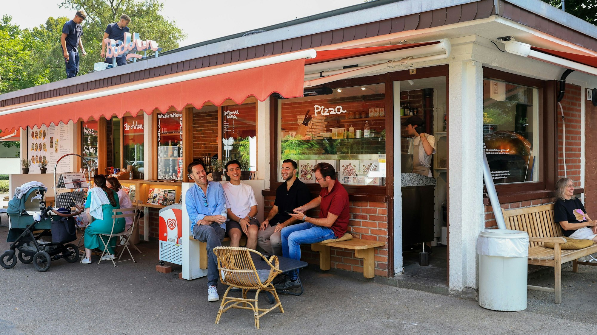 Das Büdchen am Südpark, davor sitzen einige Leute auf Bänken.