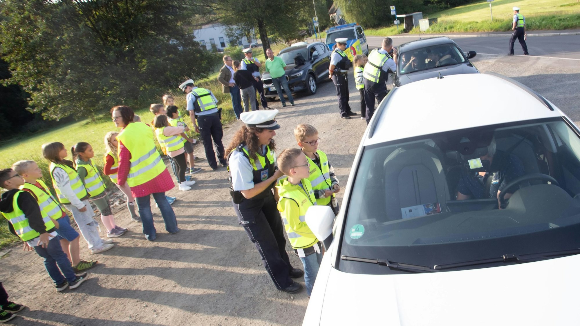 Viele Kinder und einige Polizisten stoppen Autos und reden mit den Fahrern.