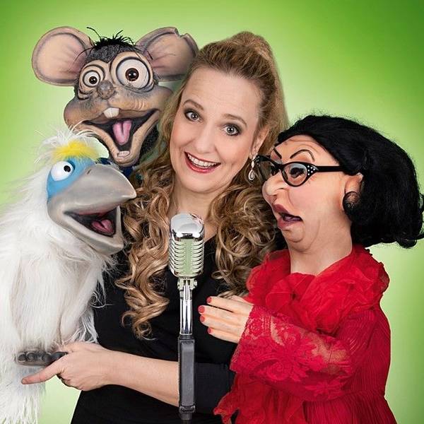 Eine Frau steht mit Puppen vor einem Mikrofon.
