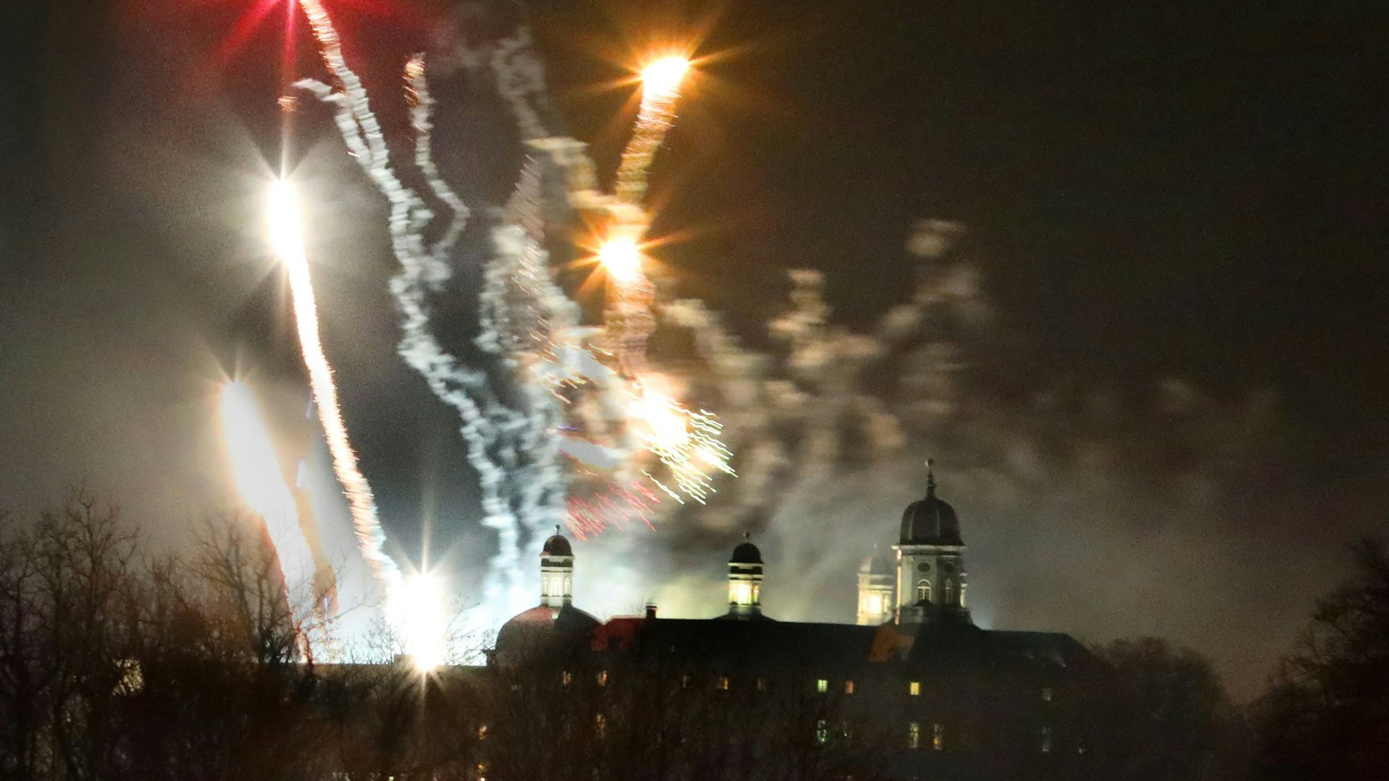 Im Vordergrund sieht man im Dunkeln die Umrisse vom Schloss Bensberg. Im Hintergrund Silvester-Raketen.