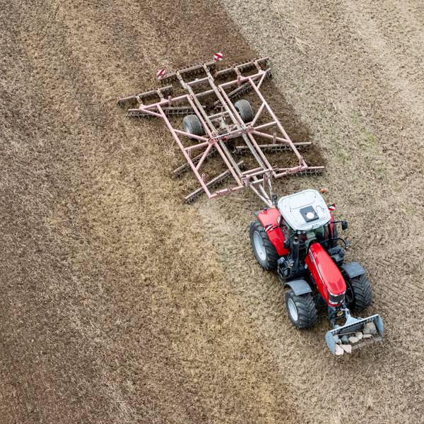 Ein Traktor mit einer Spatenrollegge fährt über ein abgeerntetes Feld.