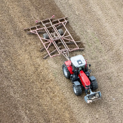 Ein Traktor mit einer Spatenrollegge fährt über ein abgeerntetes Feld.