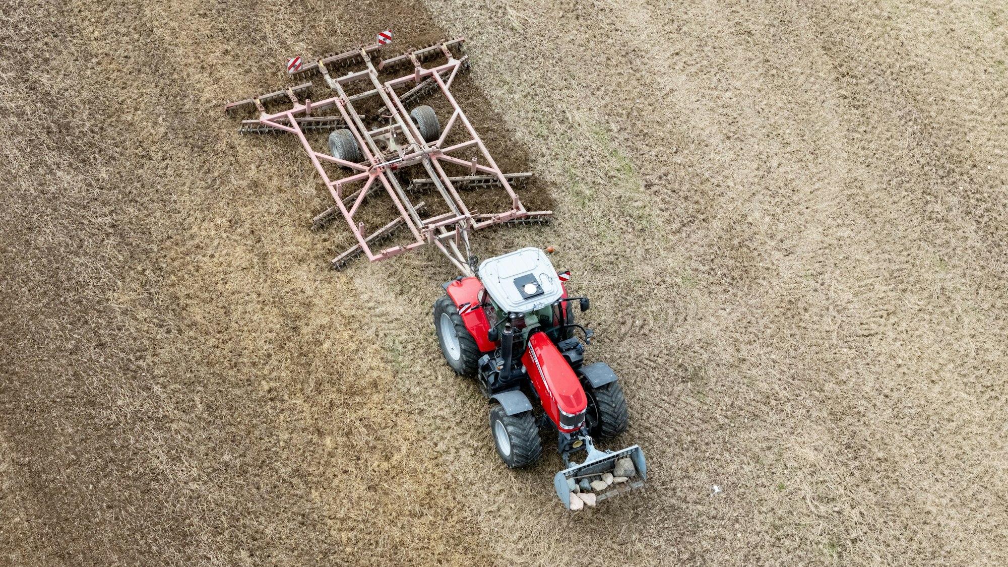 Ein Traktor mit einer Spatenrollegge fährt über ein abgeerntetes Feld.