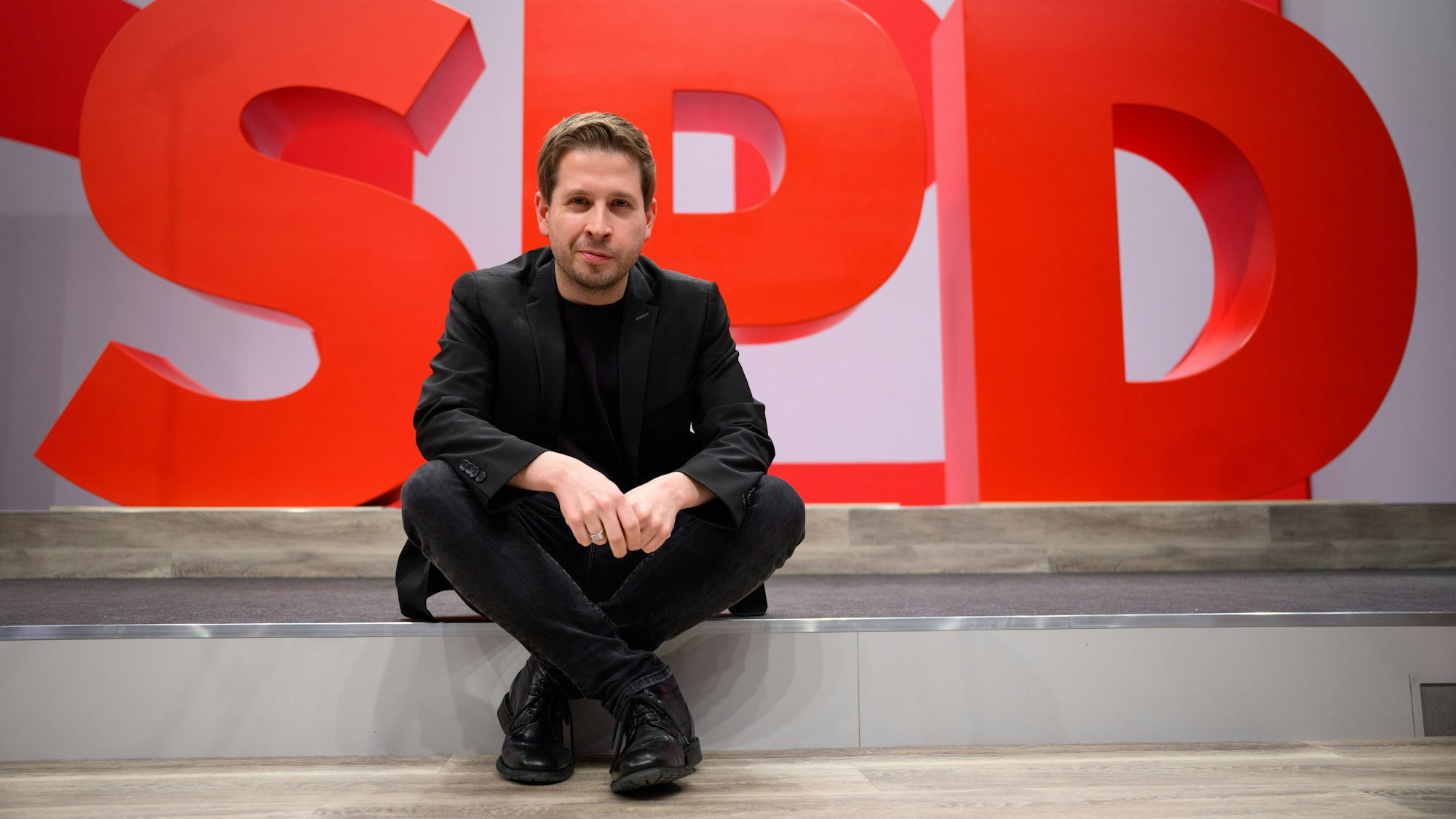 Kevin Kühnert, SPD-Generalsekretär, sitzt im Vorfeld des ordentlichen Bundesparteitags der SPD bei einem Hallenrundgang durch den Tagungsort vor einem SPD-Logo. (Archivbild)