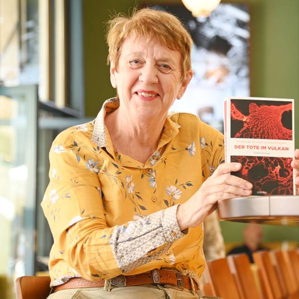 Eine Frau sitzt mit einem Krimi an der Theke eines Cafés.