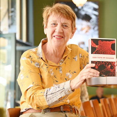 Eine Frau sitzt mit einem Krimi an der Theke eines Cafés.