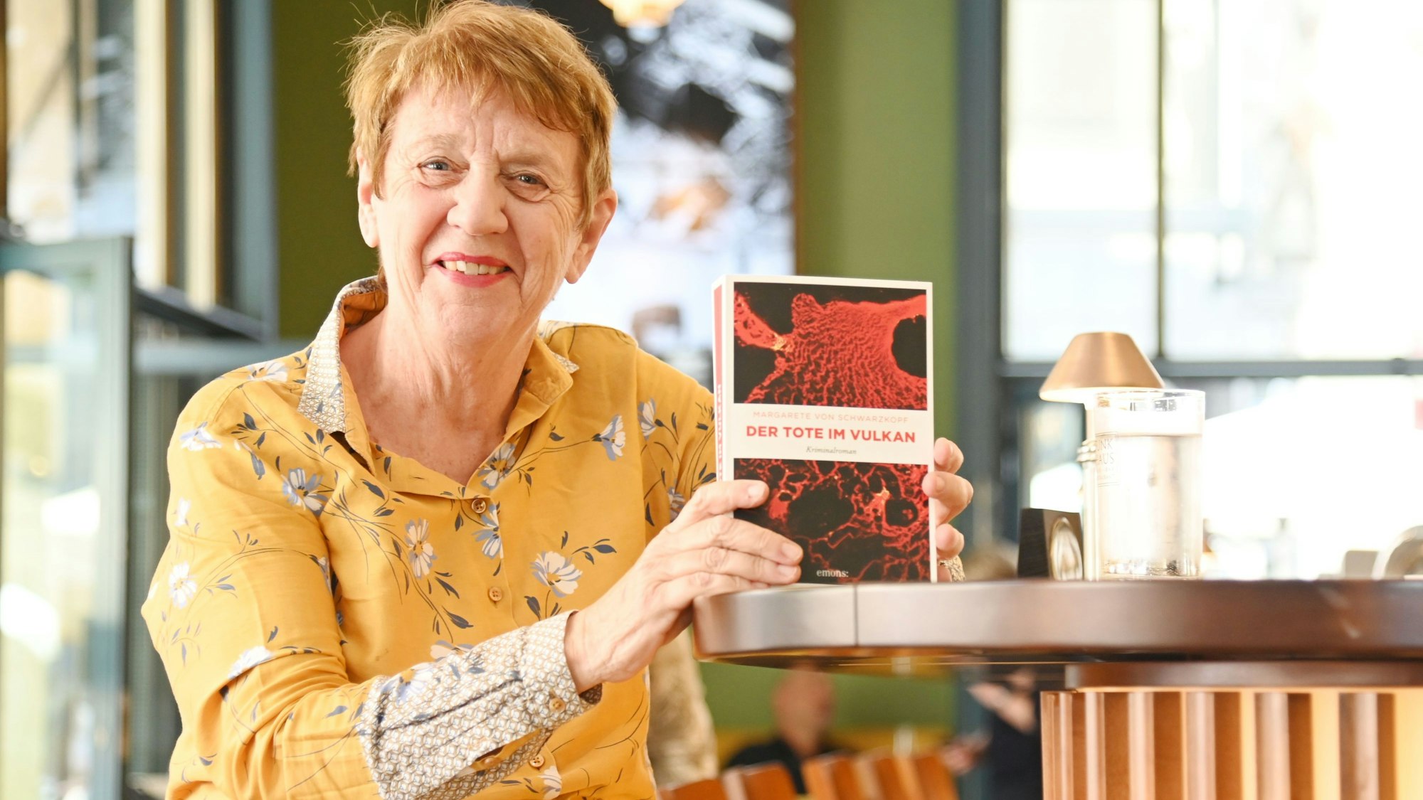 Eine Frau sitzt mit einem Krimi an der Theke eines Cafés.