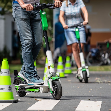Teilnehmer an einem Fahrsicherheitstraining für Elektro-Tretroller fahren auf einem Verkehrsübungsplatz um die Pylonen (Symbolbild)
