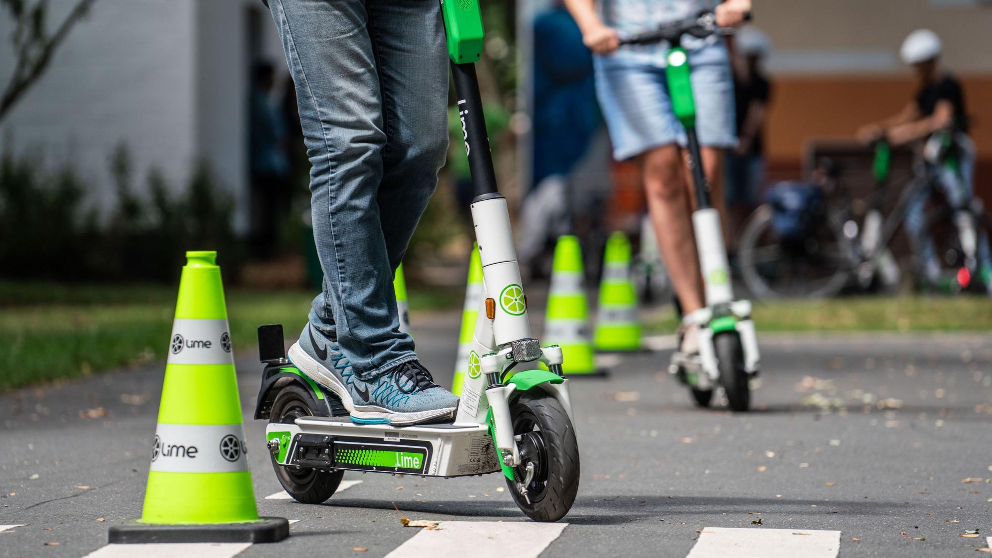 Teilnehmer an einem Fahrsicherheitstraining für Elektro-Tretroller fahren auf einem Verkehrsübungsplatz um die Pylonen