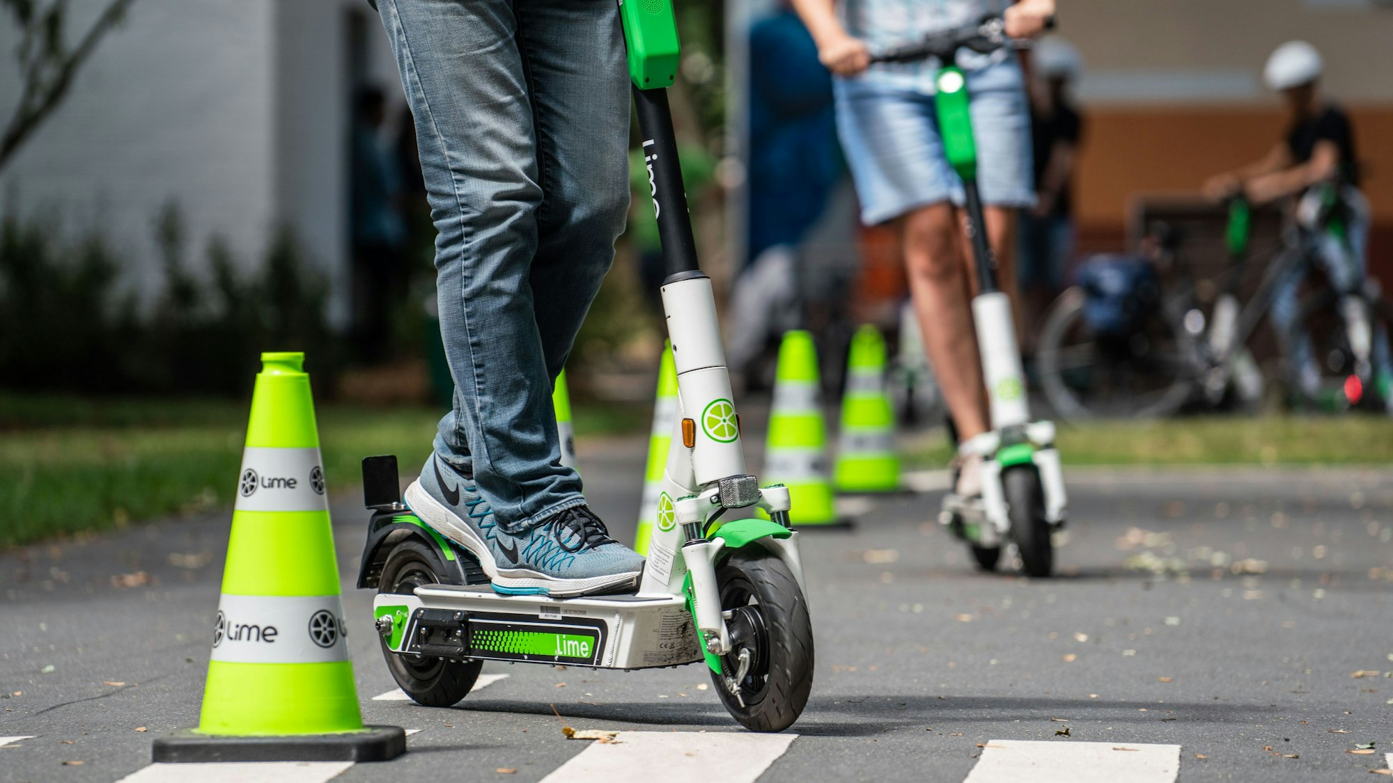 Teilnehmer an einem Fahrsicherheitstraining für Elektro-Tretroller fahren auf einem Verkehrsübungsplatz um die Pylonen