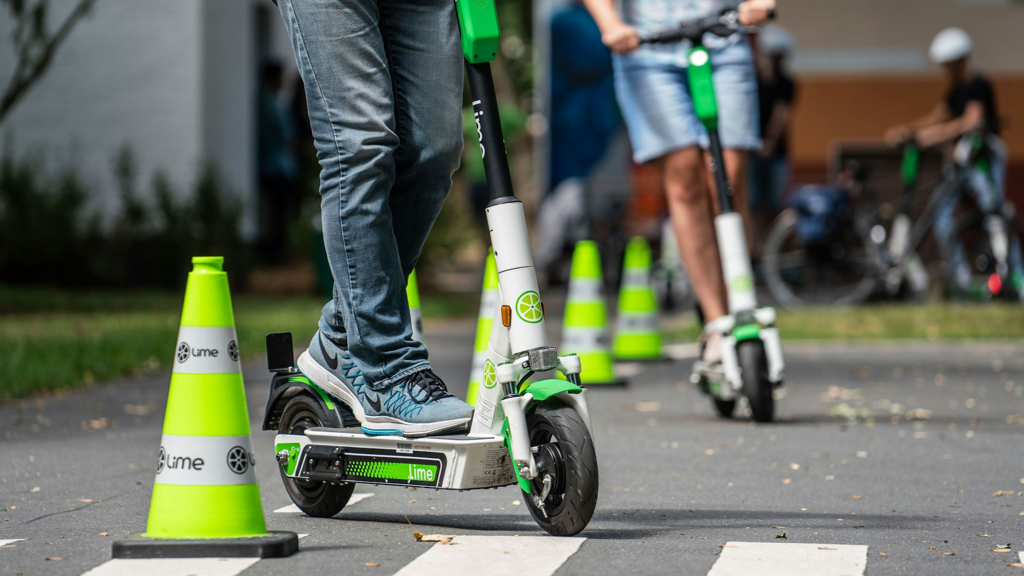 Teilnehmer an einem Fahrsicherheitstraining für Elektro-Tretroller fahren auf einem Verkehrsübungsplatz um die Pylonen (Symbolbild)