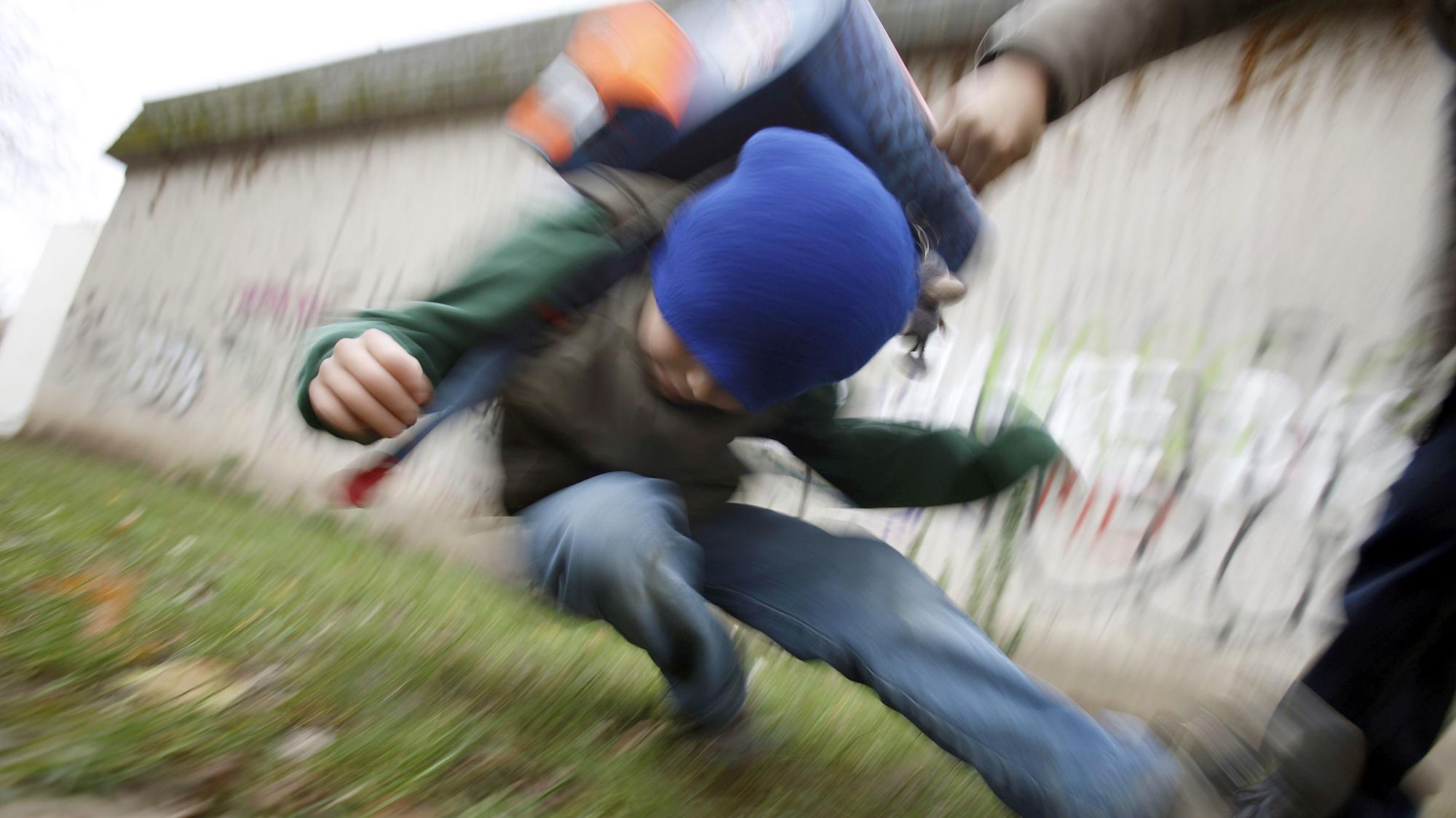 Ein Schüler drückt auf dem Schulhof eines Gymnasiums einen anderen Schüler zu Boden (gestelltes Illustrationsfoto).