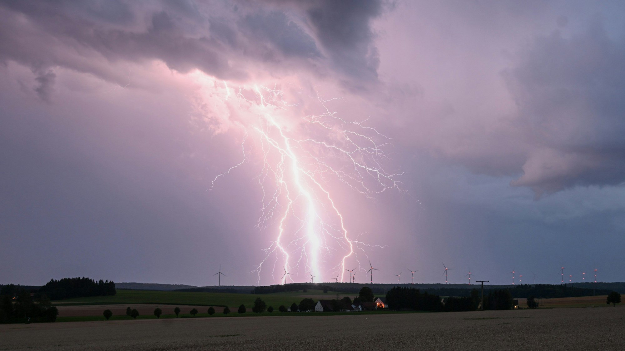 Ein Blitz zuckt bei einem Sommergewitter am abendlichen Himmel über Bartholomä auf der Schwäbischen Alb.