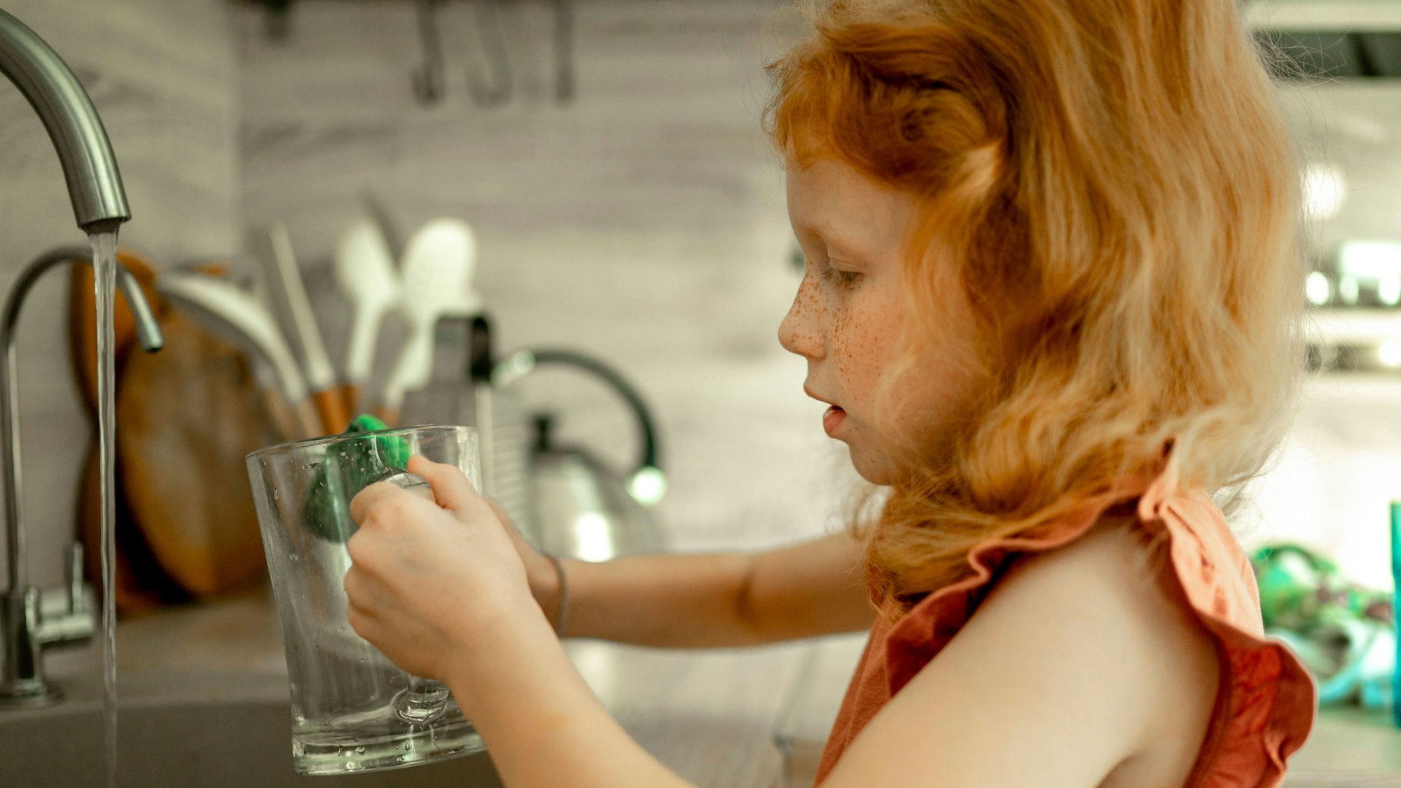 Ein kleines Mädchen mit roten Haaren steht am Spülbecken und macht den Abwasch.
