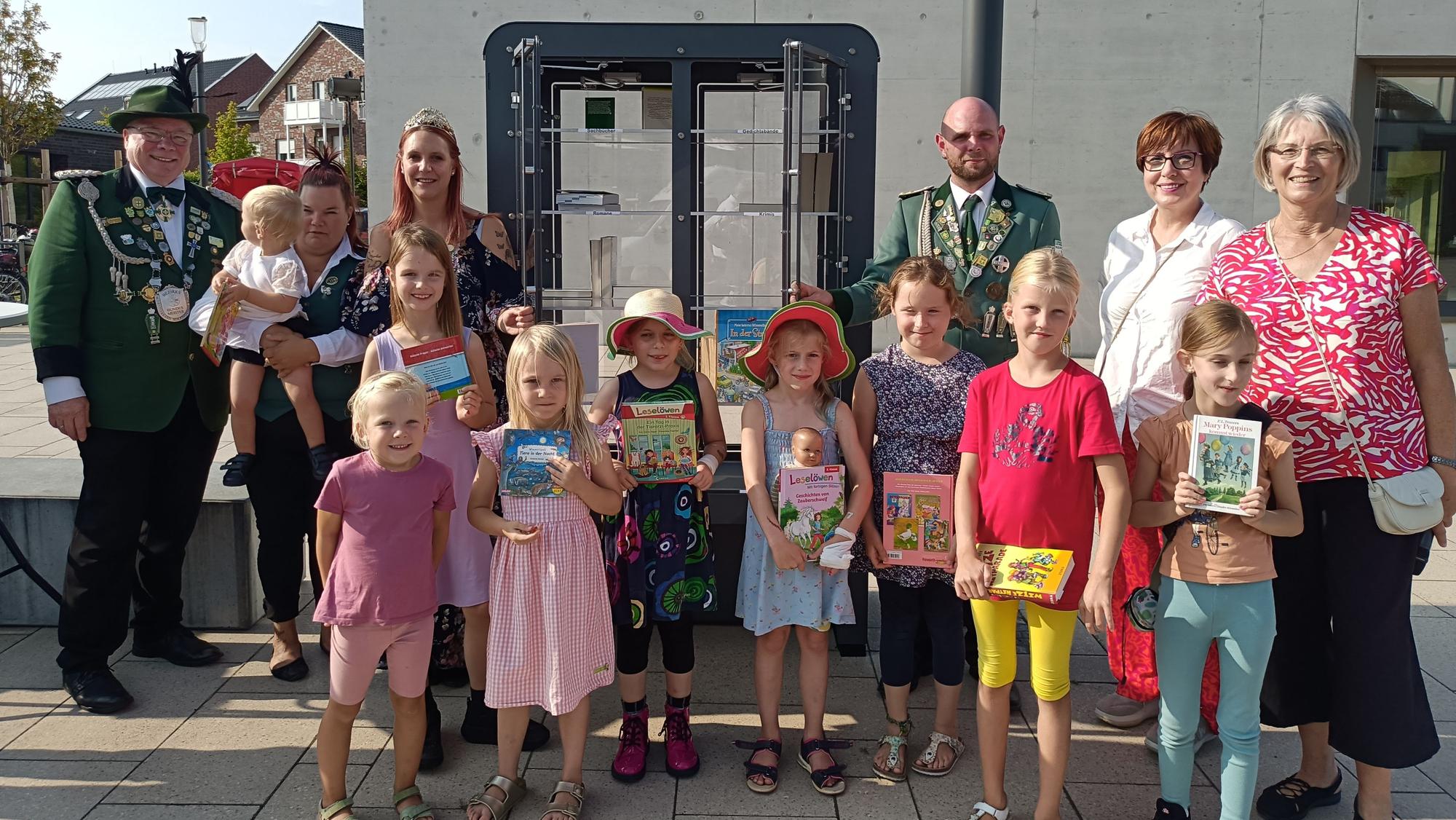 Kinder und Erwachsene stehen vor einem Bücherschrank.