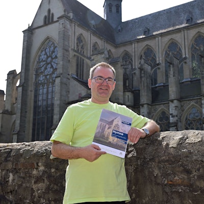 Domorganist Rolf Müller vor dem Altenberger Dom. In den Händen hält er ein Heft mit der Aufschrift "Hymne".