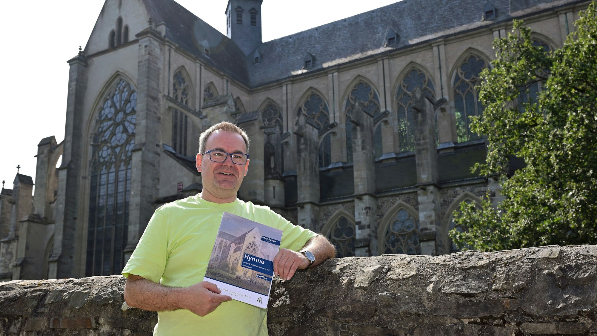 Domorganist Rolf Müller vor dem Altenberger Dom. In den Händen hält er ein Heft mit der Aufschrift "Hymne".