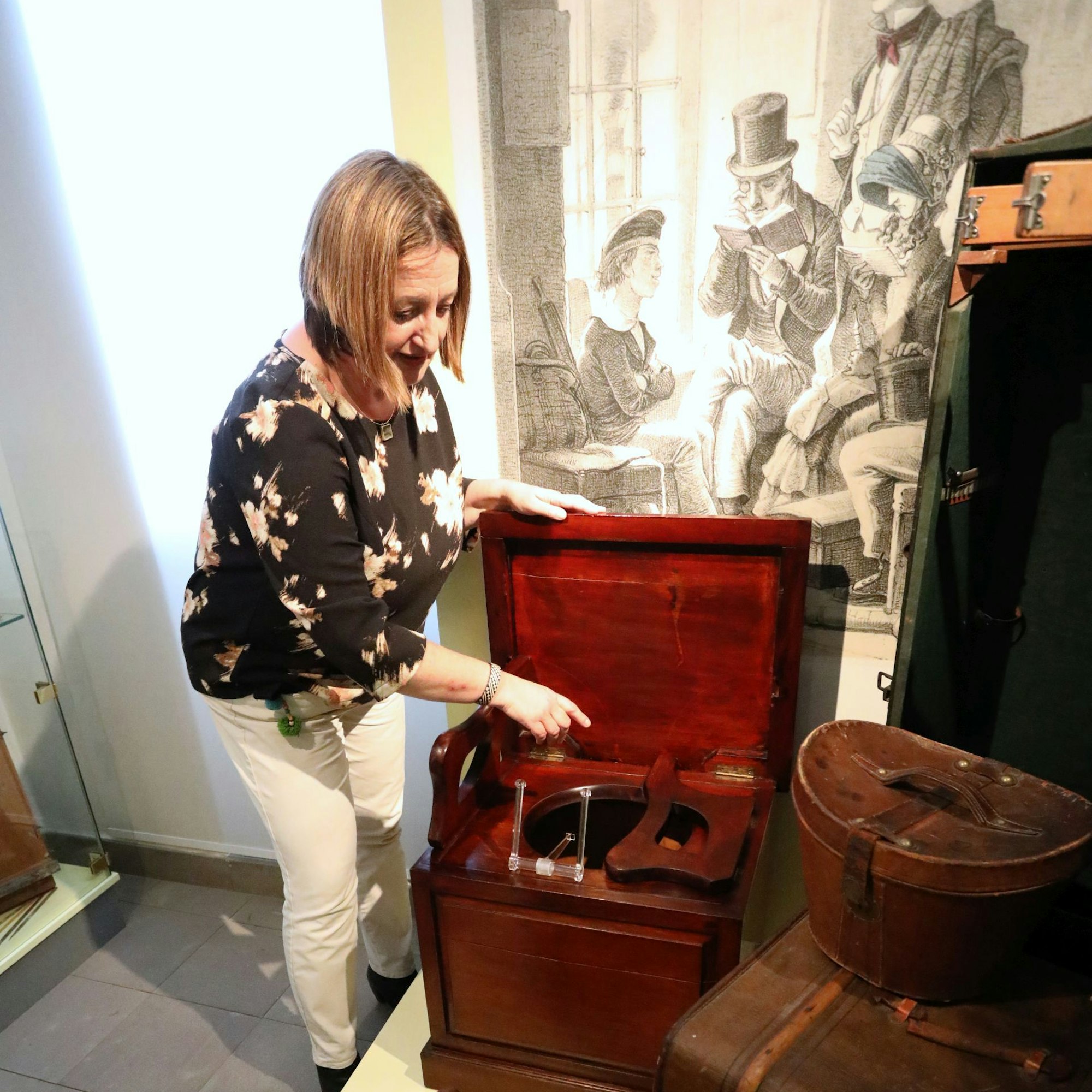 Eine Frau mit historischen Koffern und Kästen sowie einer Reisetoilette aus dem 19. Jahrhundert.