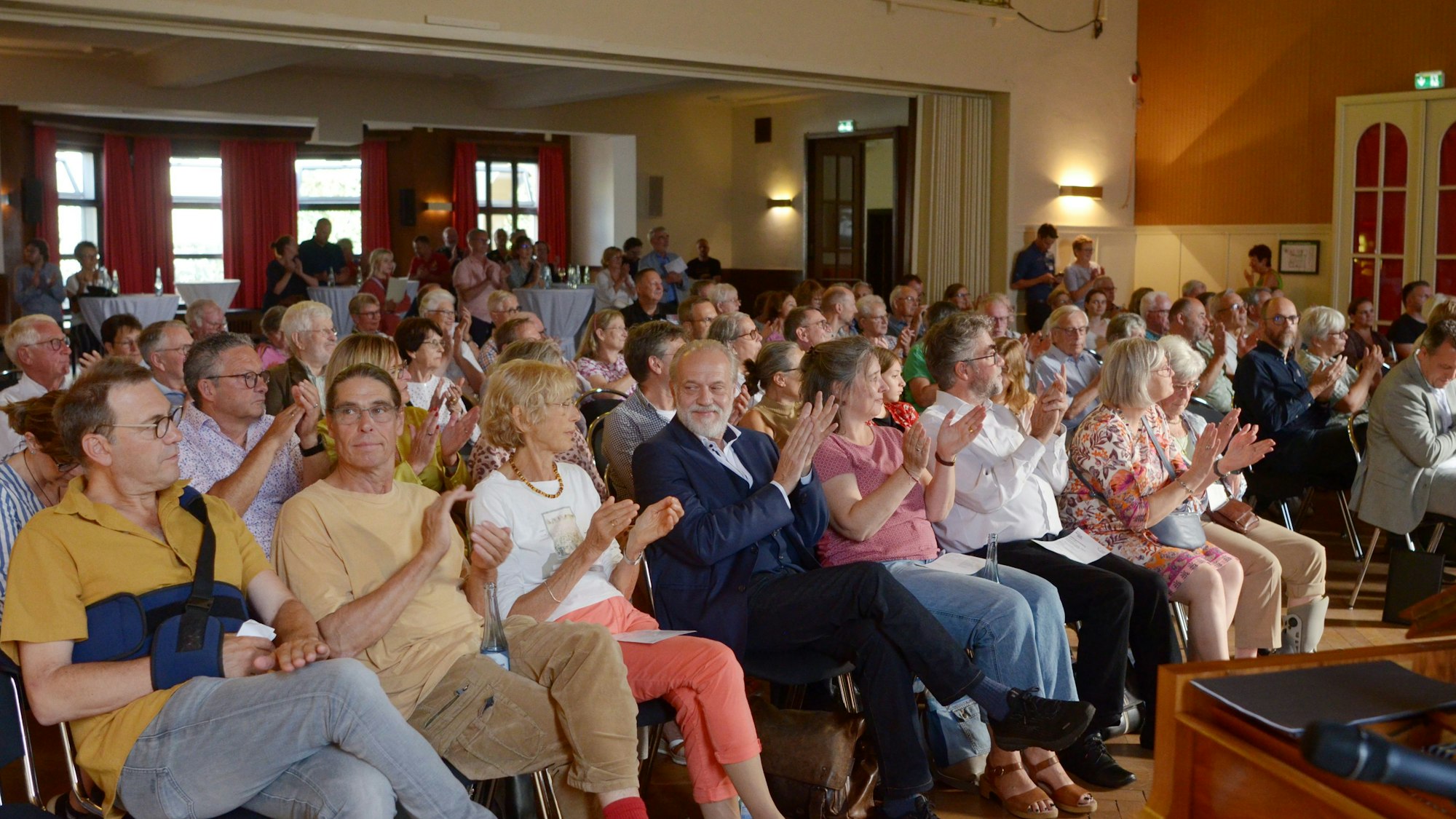 Die Gäste sitzen in Stuhlreihen im Casino und applaudieren.