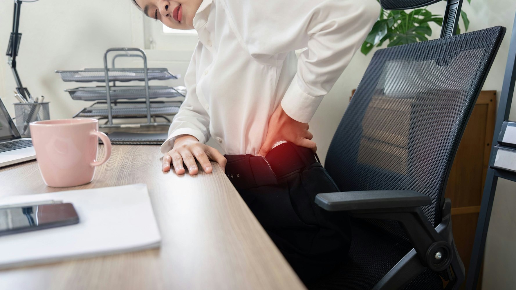Im Büro sitzende Frau fasst sich an den Rücken