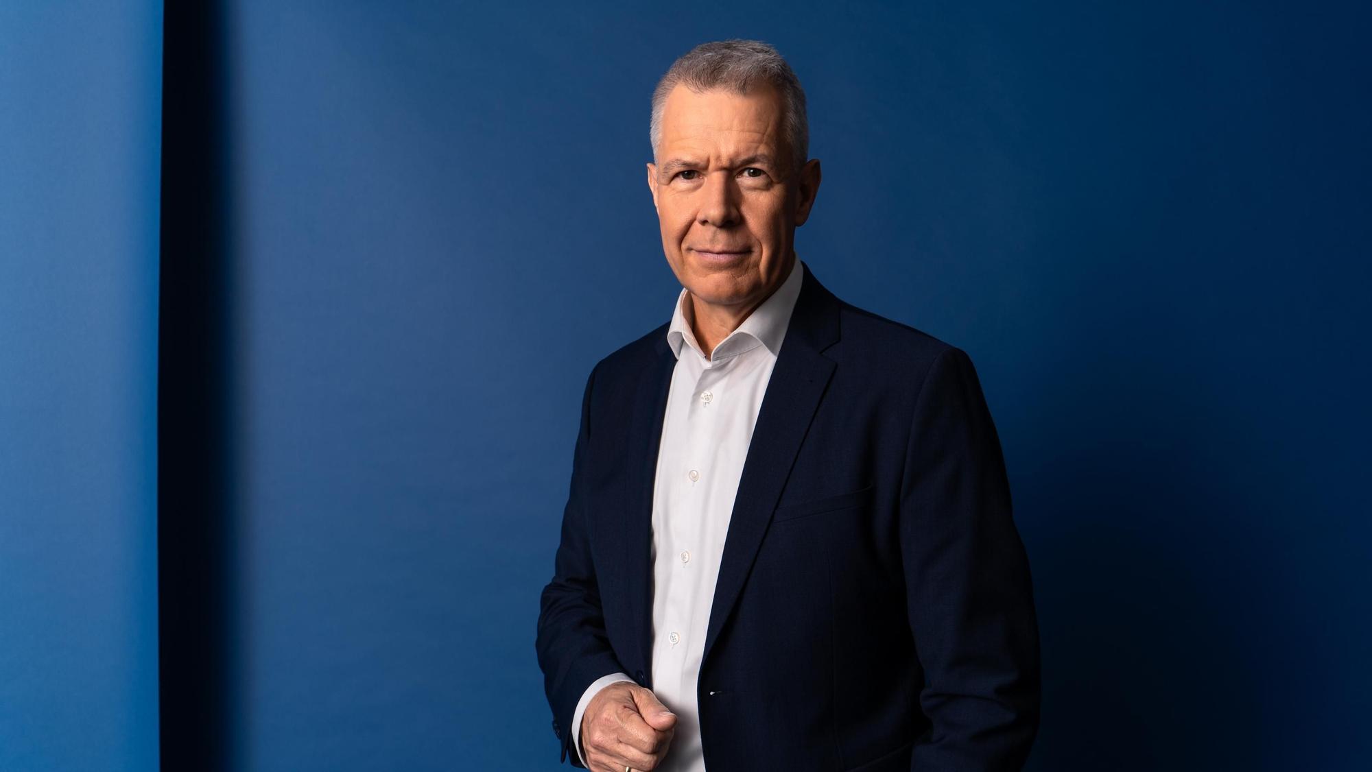 Peter Kloeppel steht in einem dunklen Anzug vor einer blauen Wand
