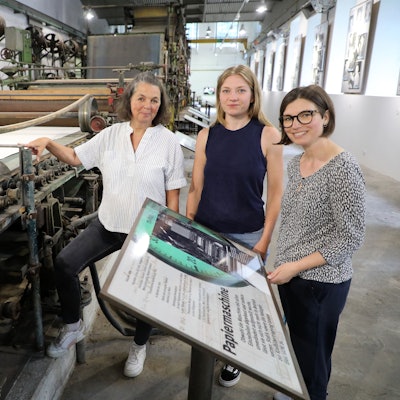 Die Museumsmacherinnen Sonja Nanko, Sophie Schmidt und Annette Schrick stehen an der Papiermaschine 4, die ab sofort wieder im Papiermuseum Alte Dombach zu sehen ist.