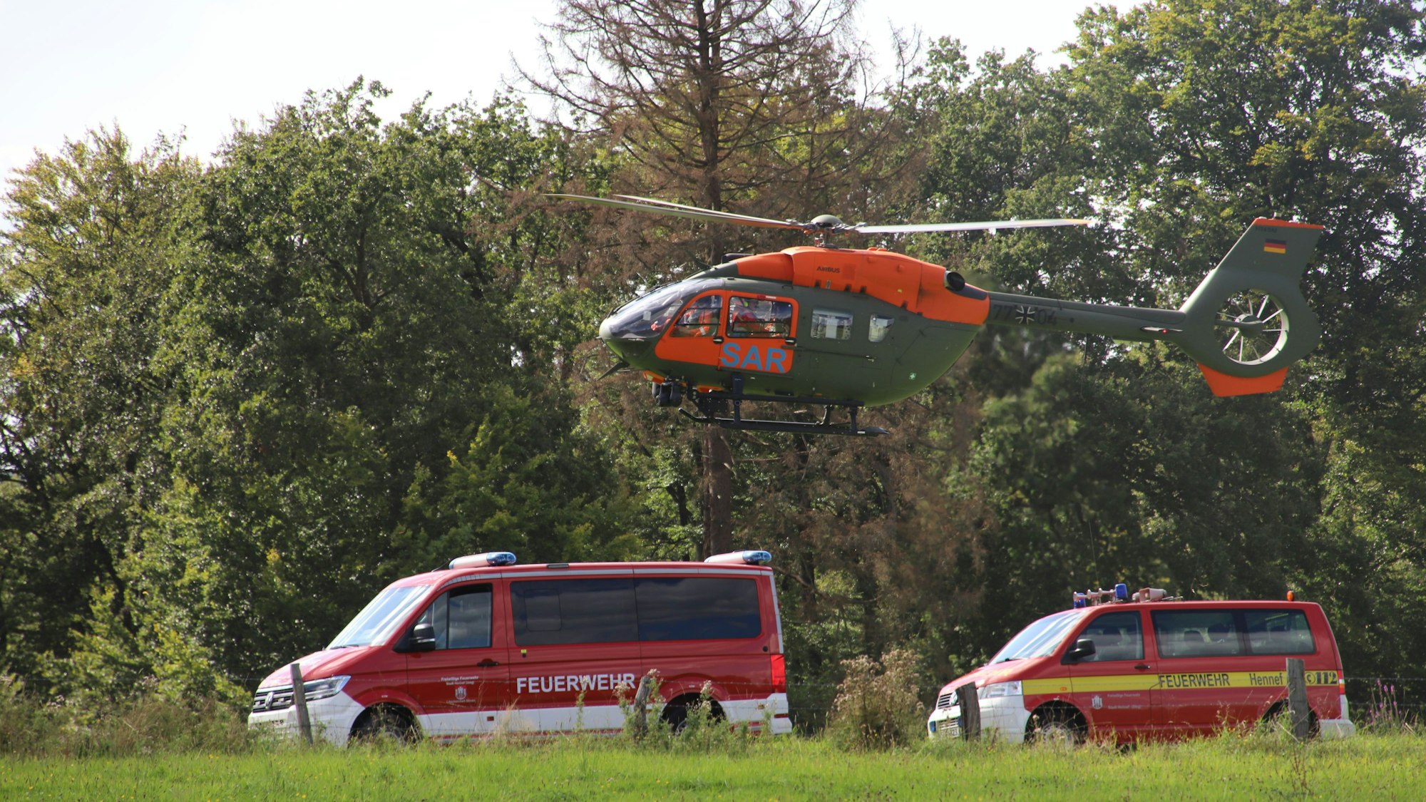 Ein Hubschrauber landet hinter zwei Feuerwehrfahrzeugen.