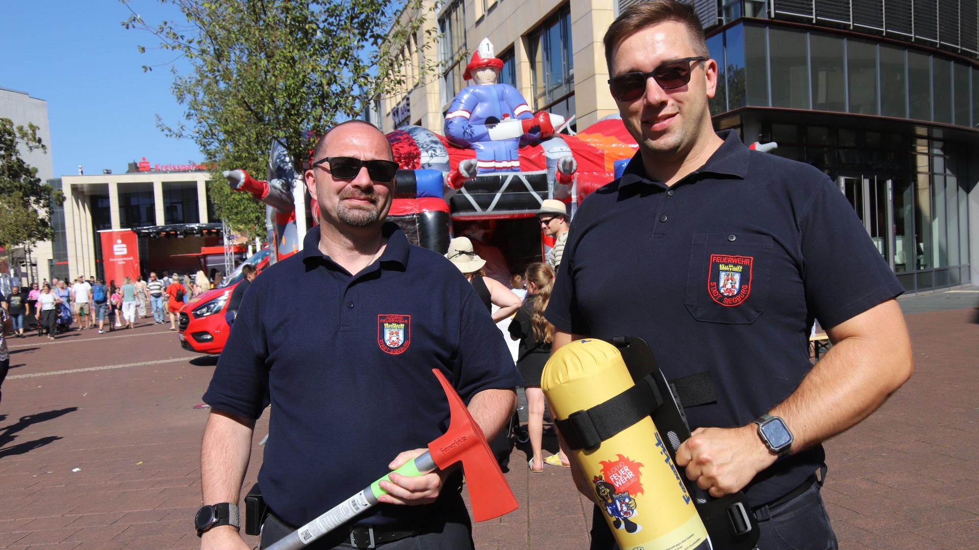 Zwei Feuerwehrleute präsentieren kindgerechtes Feuerwehr-Equipment.