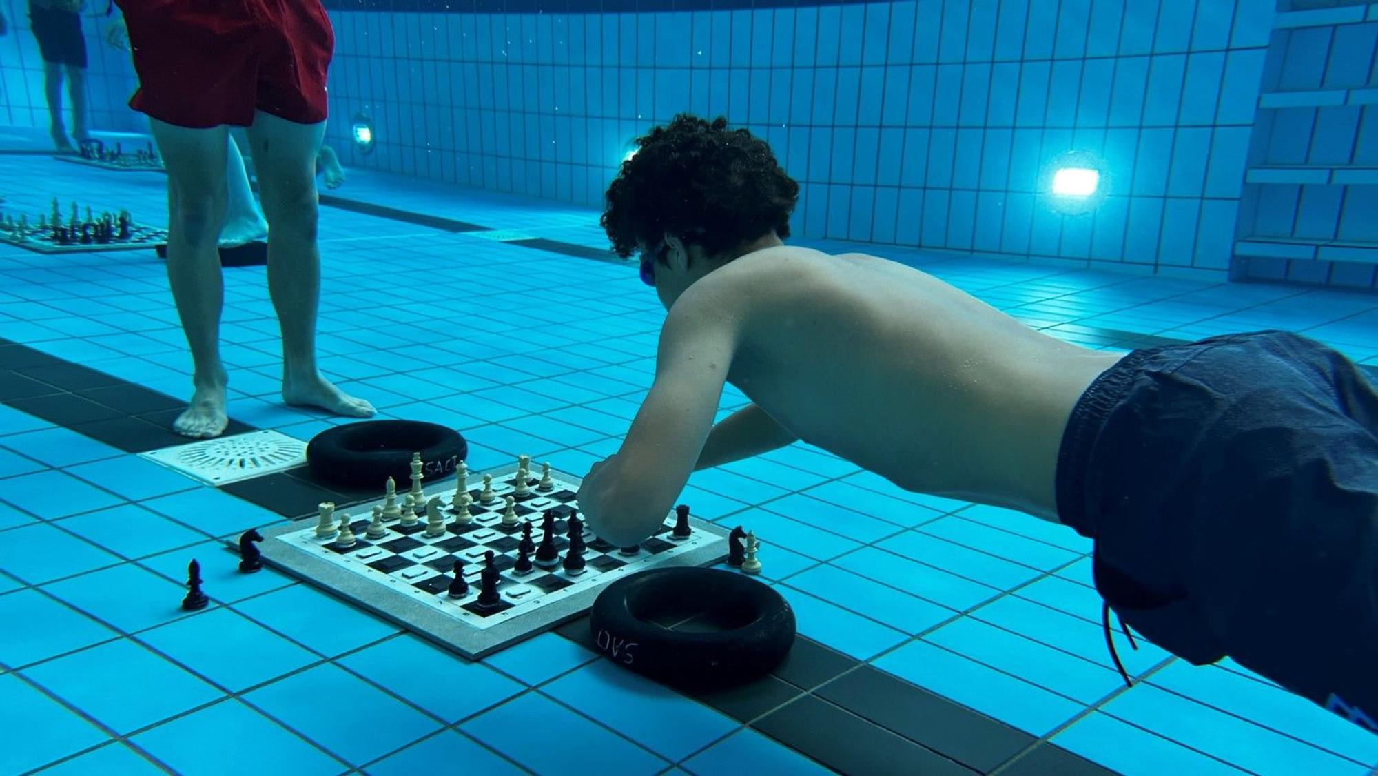 Ein Schachspieler taucht im Schwimmbecken ab, um beim Unterwasserschach einen Zug zu machen.