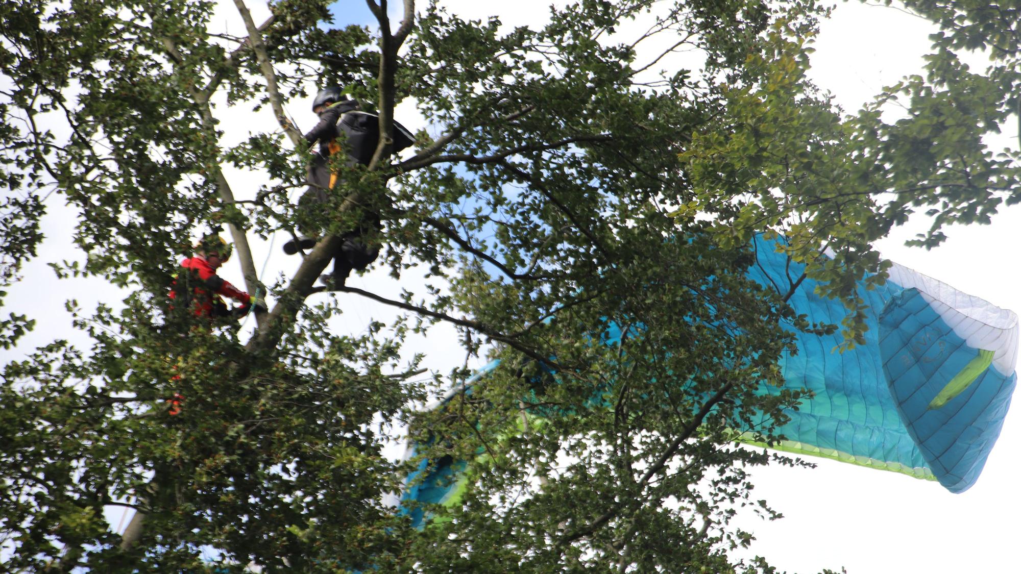 Ein Gleitschirmflieger hängt im Baum, ein Feuerwehrmann ist bei ihm.