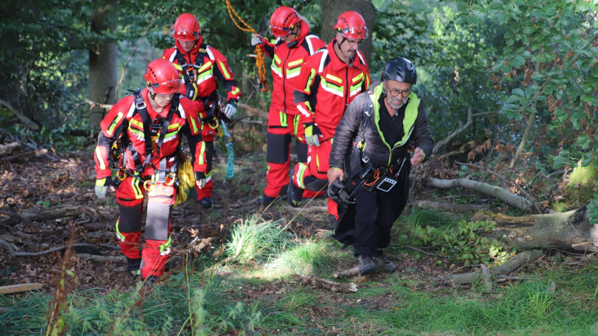 Vier Feuerwehrleute begleiten einen Gleitschirmflieger zum Rettungsdienst.