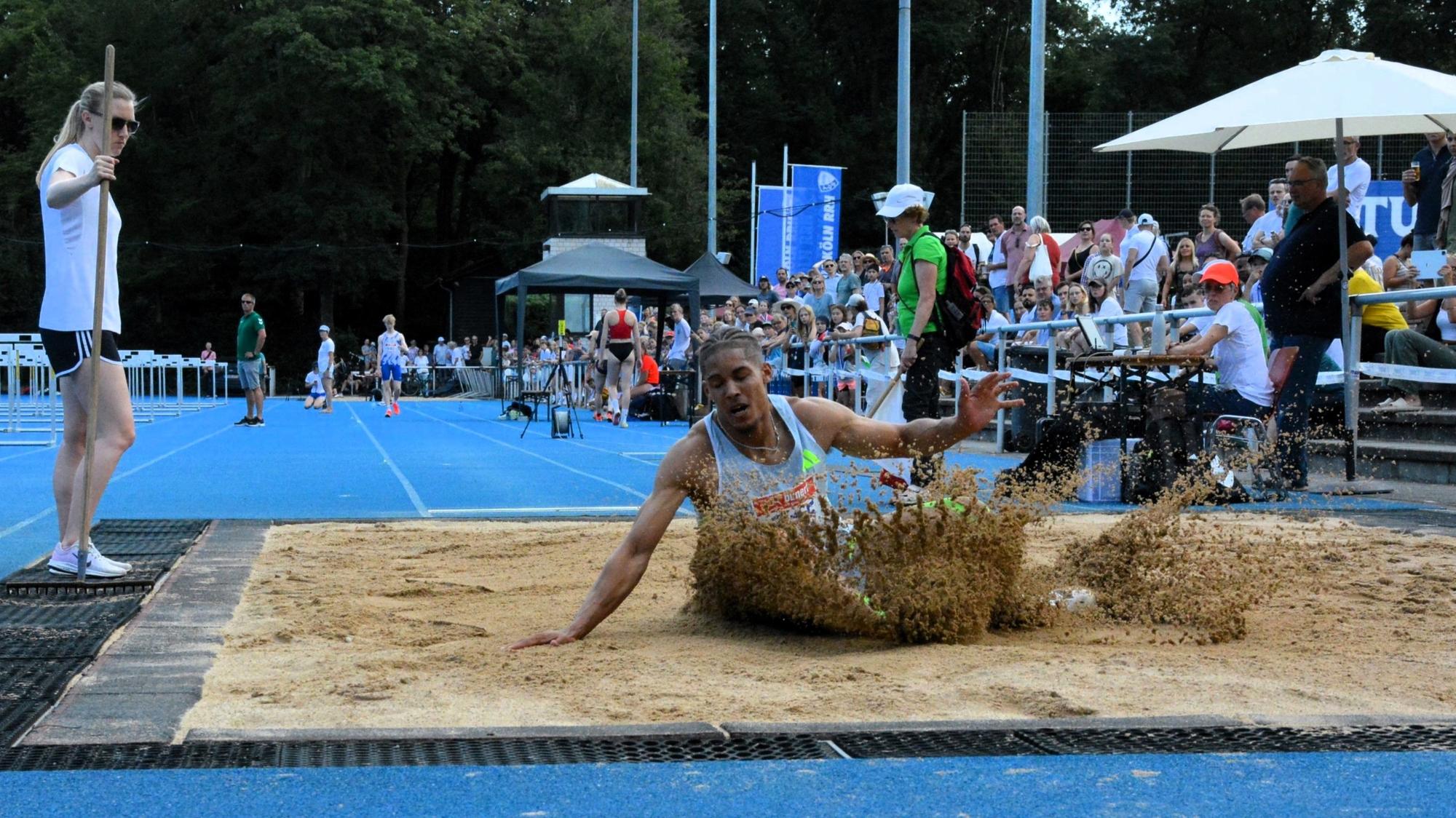 Ein Weitspringer landet in der Grube und Sand spritzt auf.
