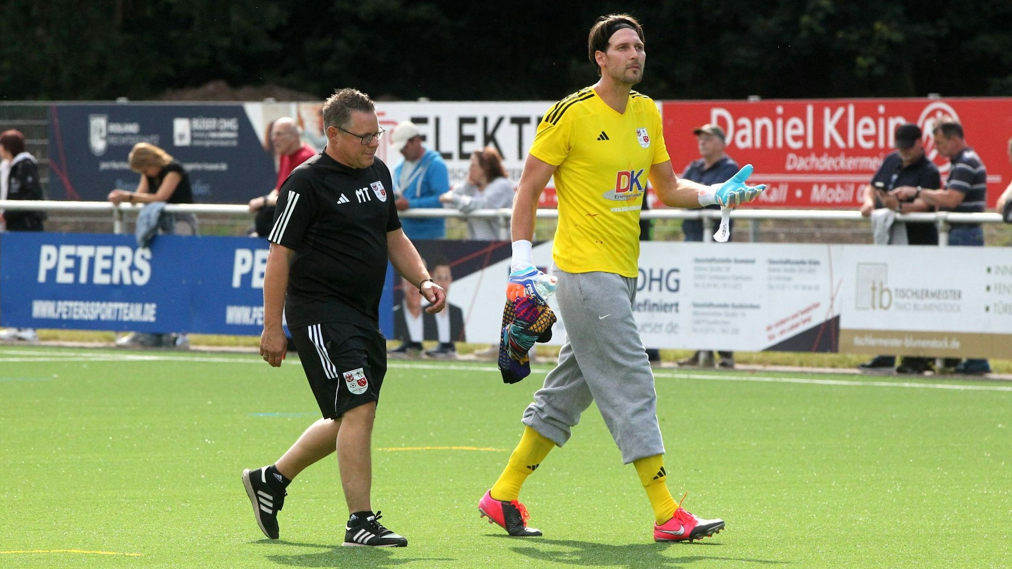 Fabien Giefer trägt eine graue Trainingshose zum gelben Trikot und gelben Stutzen. Neben ihm Trainer Marcel Timm.