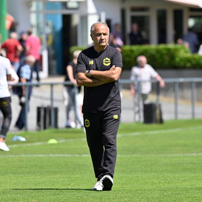 Bild eines Fußballtrainers, der allein über den Rasen geht.