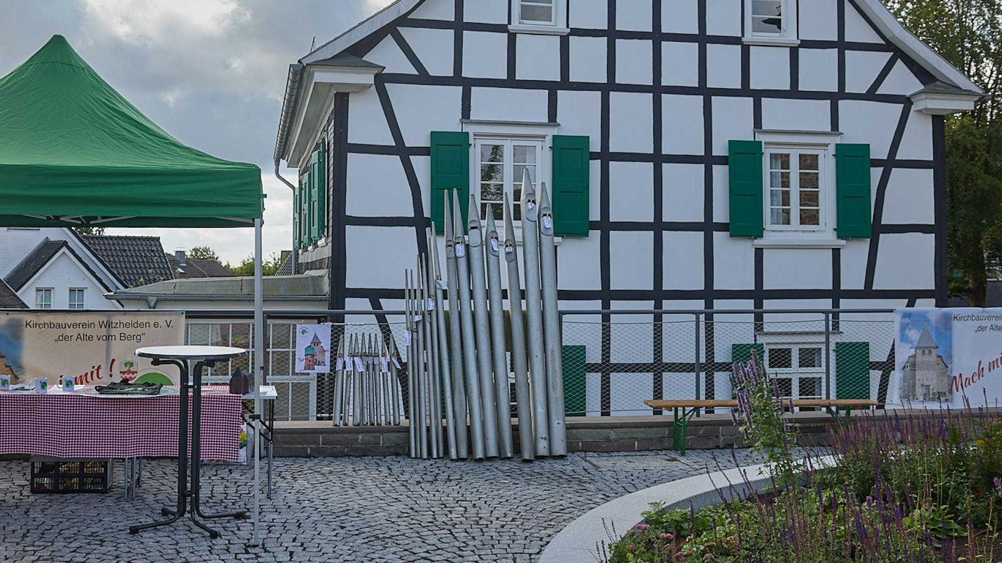 Orgelpfeifen stehen vor einem Fachwerkhaus.