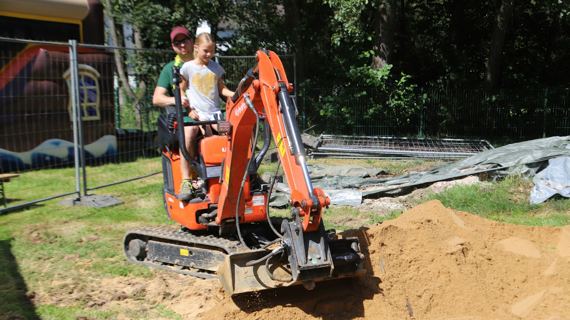 Ein Gartenbauer fährt mit einem Mädchen Bagger.
