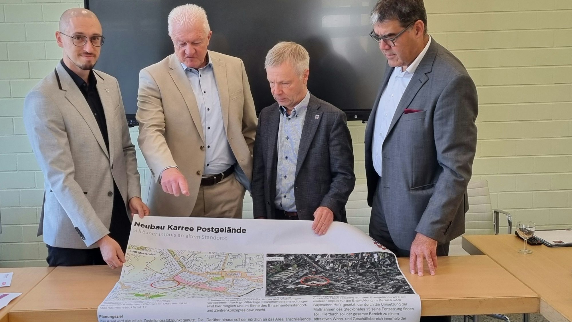 Vier Männer stehen vor einem großformatigen Plan.