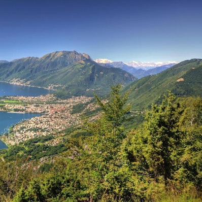 Panoramablick über einen alpinen Lago Maggiore mit Berg und Stadtbild an einem sonnigen Sommertag über Locarno.
