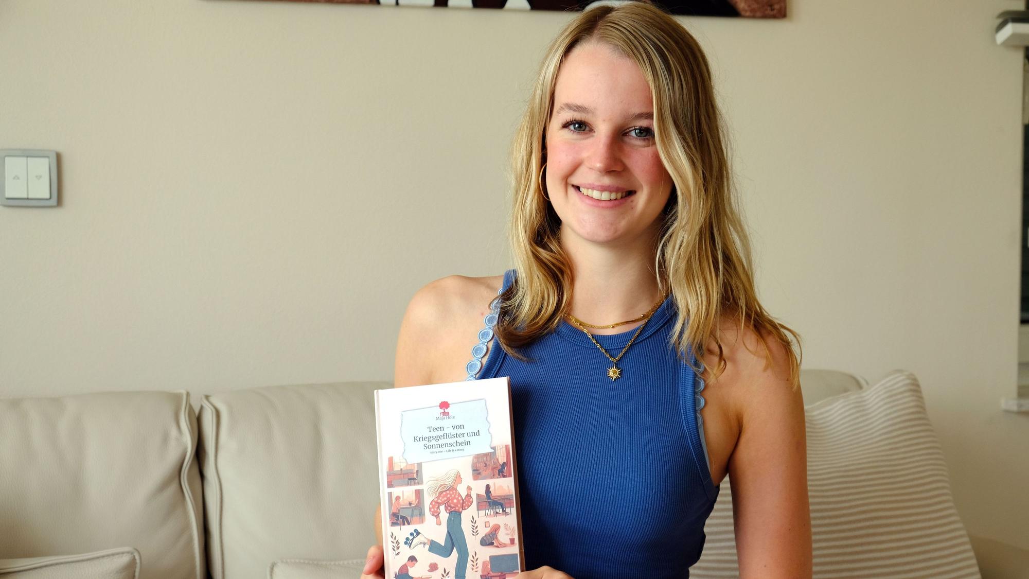 Maja Hölz sitzt auf einem Sofa und hält vor sich ihr Buch.