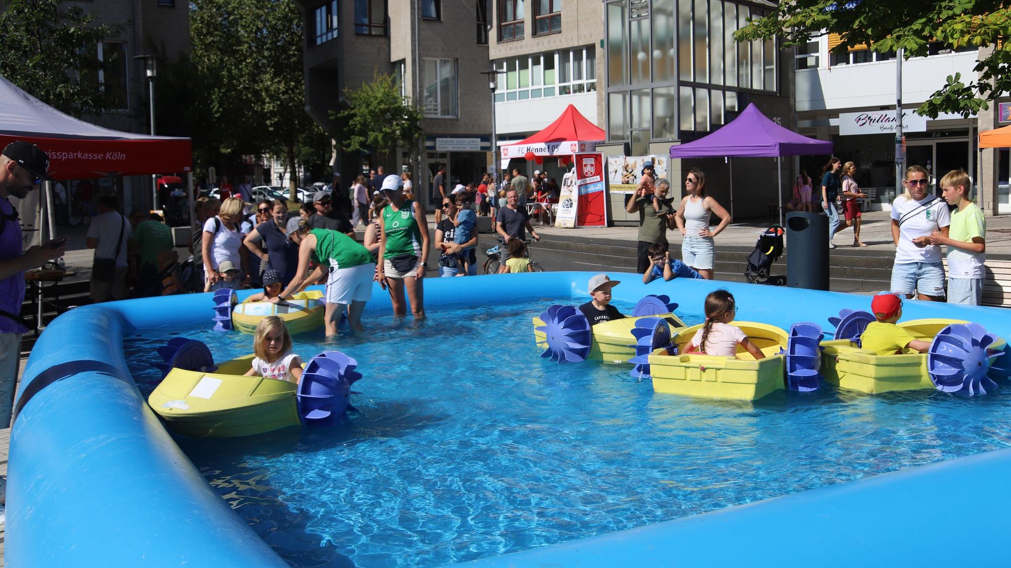 Kinder sitzen in kleinen Schaufelrad-Booten in einem Bassin, das auf dem Marktplatz aufgebaut wurde.