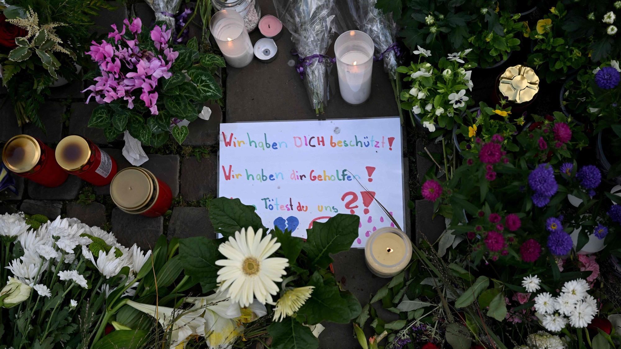 Auf einem Schild inmitten von Blumen und Kerzen ist zu lesen: „Wir haben dich beschützt. Wir haben dir geholfen. Tötest du uns?“