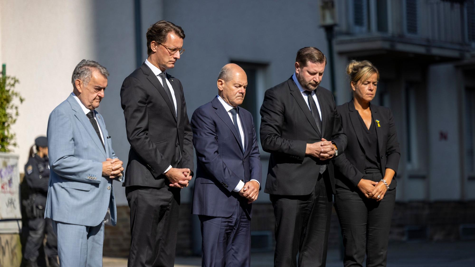 26.08.2024, Nordrhein-Westfalen, Solingen: Herbert Reul (CDU, l-r), Innenminister von Nordrhein-Westfalen, Hendrik Wüst (CDU), Ministerpräsident von Nordrhein-Westfalen, Bundeskanzler Olaf Scholz (SPD), Tim Kurzbach (SPD), Bürgermeister von Solingen, und Mona Neubaur (Grüne), stellvertretende Ministerpräsidentin von Nordrhein-Westfalen, stehen mit gefalteten Händen vor Blumen, die in Gedenken an die Opfer niedergelegt wurden. Bei einer Messerattacke auf der 650-Jahr-Feier der Stadt Solingen am 23. August hatte es drei Todesopfer und Verletzte gegeben. Foto: Thomas Banneyer/dpa +++ dpa-Bildfunk +++