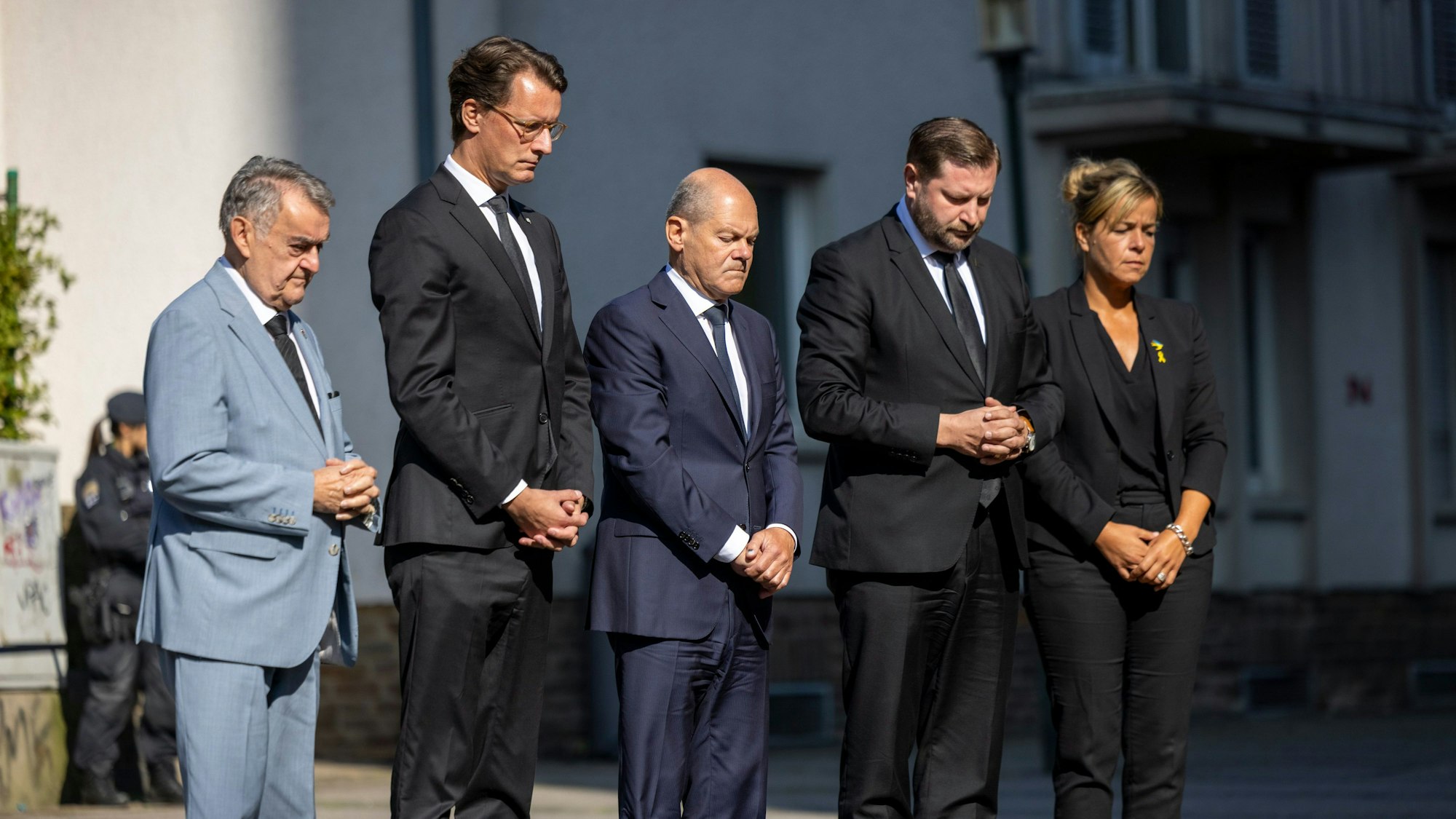 Herbert Reul (CDU, l-r), Innenminister von Nordrhein-Westfalen, Hendrik Wüst (CDU), Ministerpräsident von Nordrhein-Westfalen, Bundeskanzler Olaf Scholz (SPD), Tim Kurzbach (SPD), Bürgermeister von Solingen, und Mona Neubaur (Grüne), stellvertretende Ministerpräsidentin von Nordrhein-Westfalen, stehen mit gefalteten Händen vor Blumen, die in Gedenken an die Opfer niedergelegt wurden.