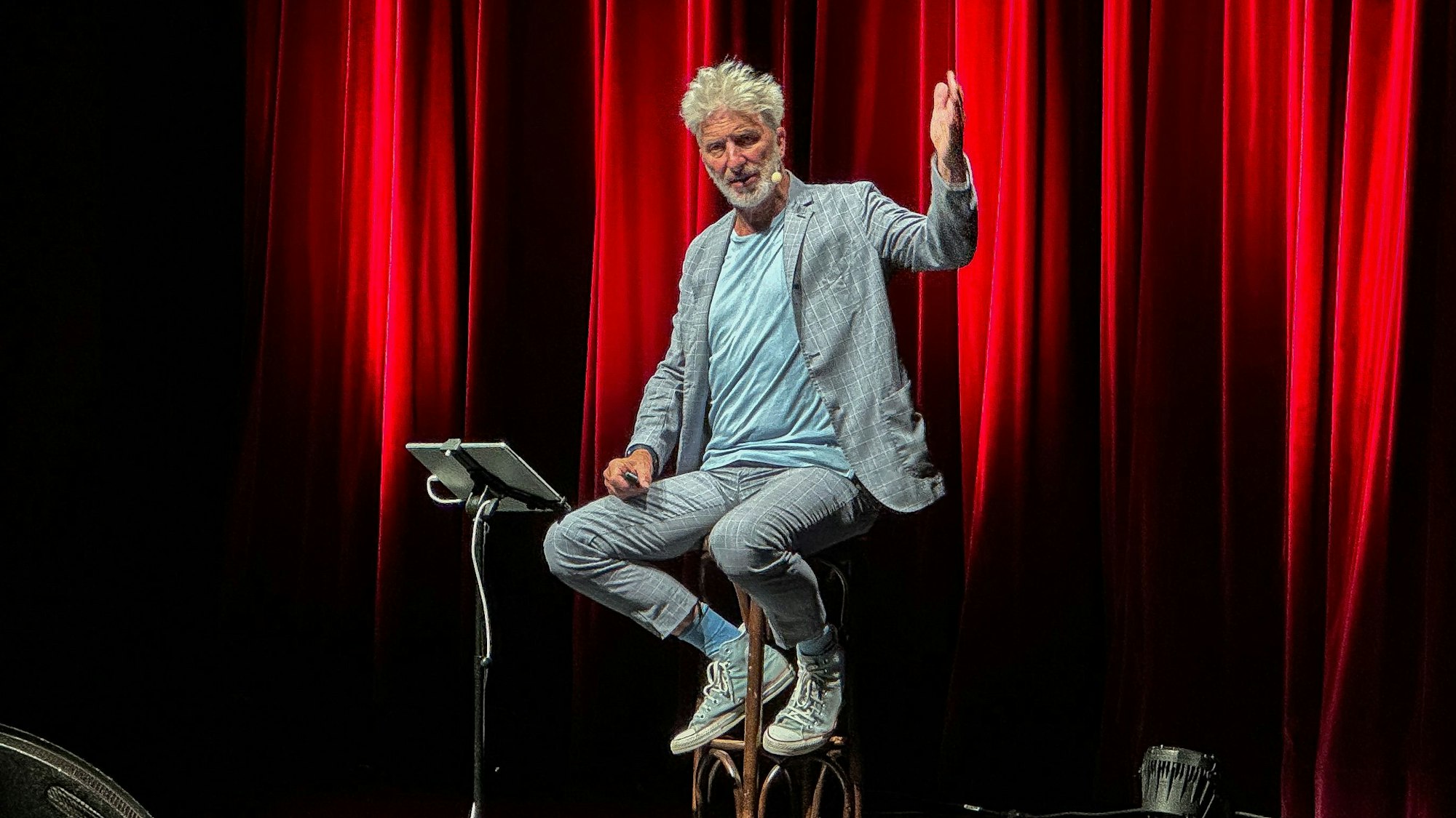 Ein Mann sitzt auf einem Hocker vor einem roten Vorhang.