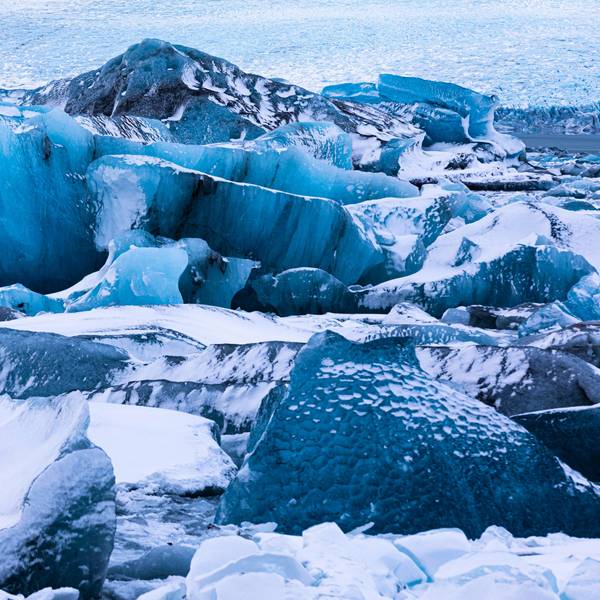 Verschneite Eisberge in der Gletscherlagune Jökullsarlon auf Island, dahinter der Breidamerkurjökull. Hier ist eine Eishöhle eingestürzt.